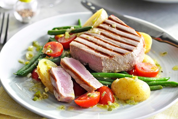 A white plate with lightly grilled tuna with Potato, tomato and green bean salad
