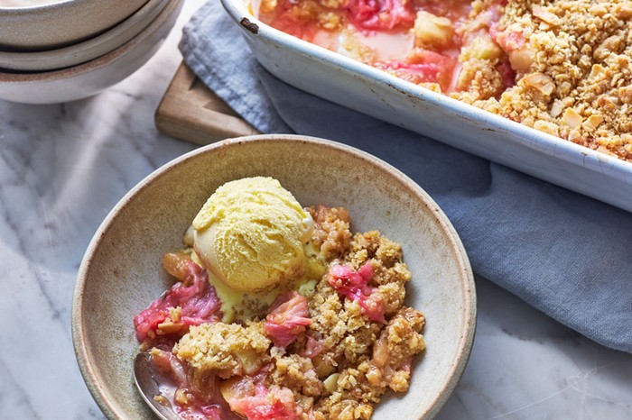 A bowl of crumble and ice cream next to a baking dish of crumble and stack of bowls