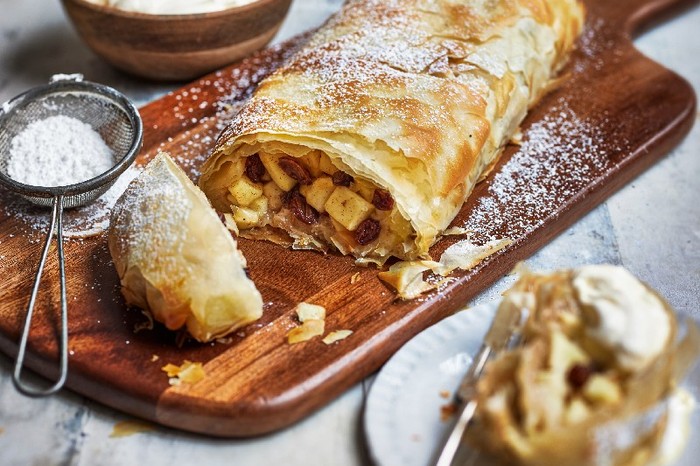 An apple strudel dusted with icing sugar on a wooden board