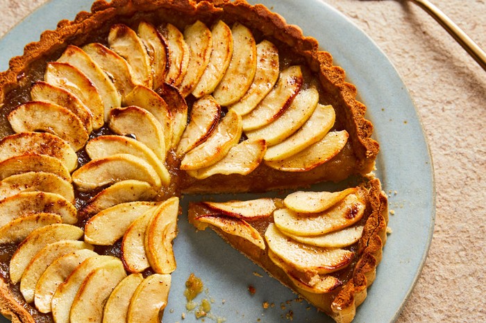 A round apple tart topped with caramelised apple pieces, with a slice taken out