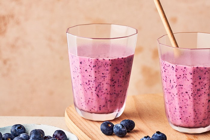 Two glasses full of blueberry smoothie on a wooden serving board