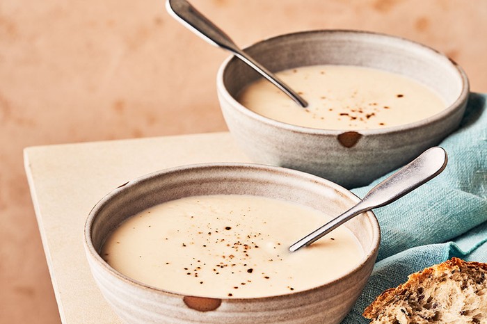 Two bowls of cauliflower soup next to some seeded bread