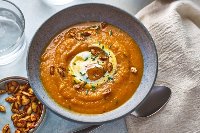 a dark grey bowl filled with orange soup with a swirl of yoghurt and toasted pumpkin seeds