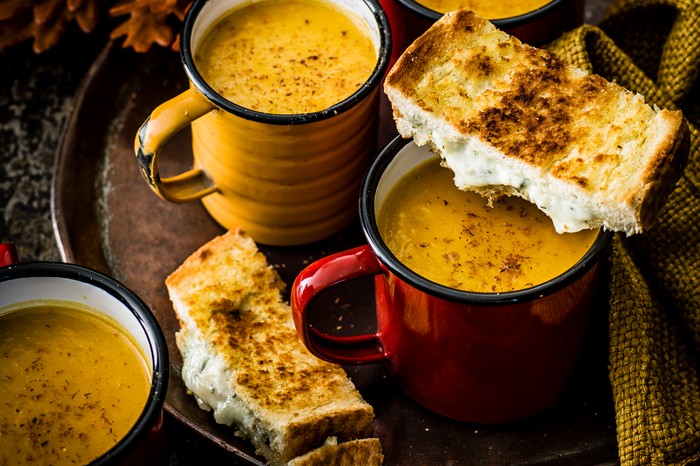 Two mugs full of pumpkin soup, next to two slices of a blue cheese toastie