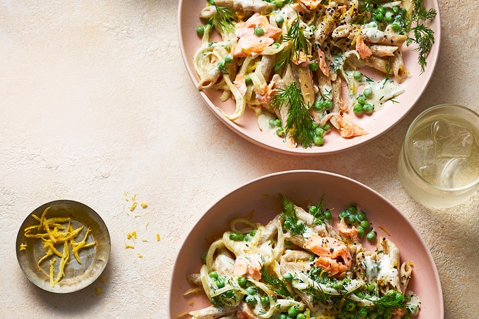 Two bowls of salmon and pea pasta with lemon zest on the side
