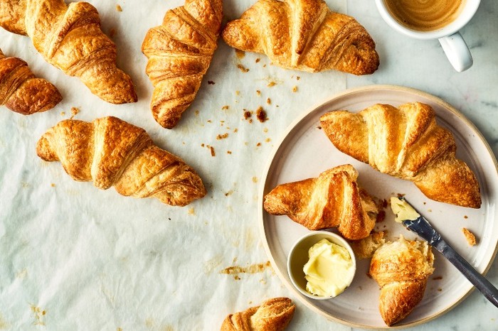 A platter of croissants with more scattered around next to it on a linen table cloth