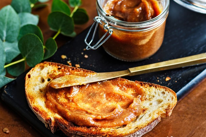 Gingerbread apple butter spread over toast on a board next to the jar