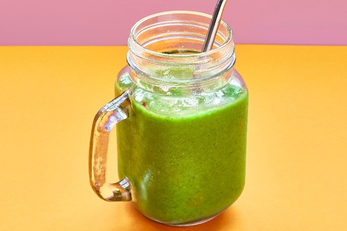 A glass filled with green kale smoothie with a metal straw on an orange and pink background