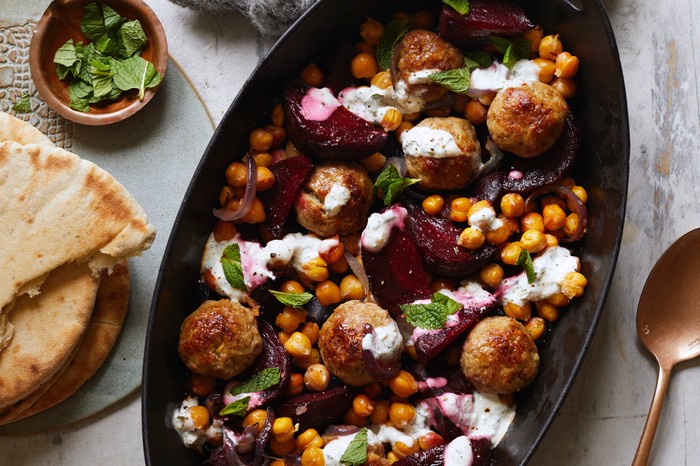 An oval-shaped black serving bowl filled with meatballs, beetroot, chickpeas and mint
