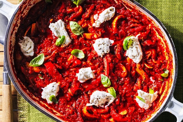 An oven dish flled with a red stew, topped with torn mozzarella next to a basket of bread