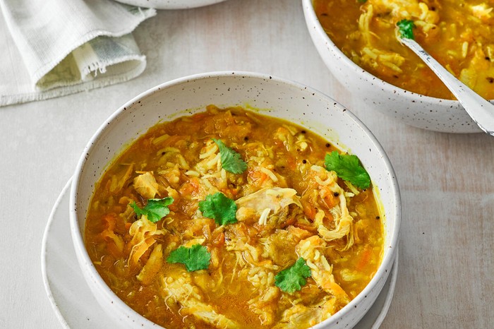 A bowl of mulligatawny soup with shredded chicken and herbs