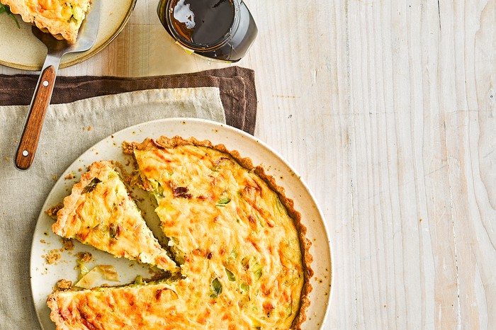 A quiche on a plate with one slice ready to be served