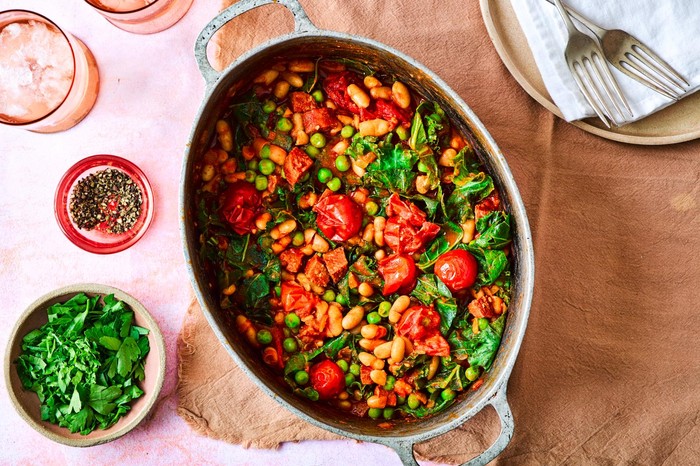Chorizo, greens and bean stew in a large dish, placed on a table with a side of chopped parsley