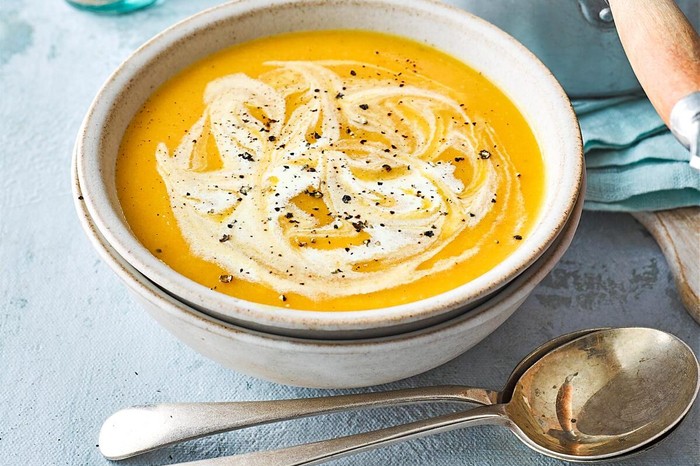 Carrot and parsnip soup in a white bowl next to spoon