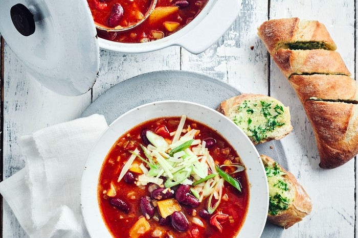 Chilli Soup Recipe served with garlic bread in a white bowl topped with chopped spring onions