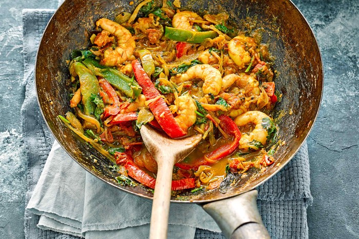 A silver wok is filled with prawns, chopped peppers and green vegetables