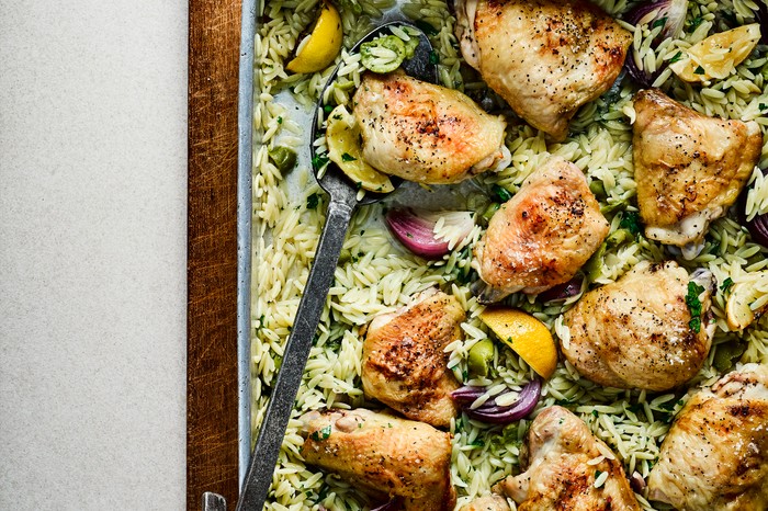 Traybake with chicken thigh pieces on a bed of orzo and olives