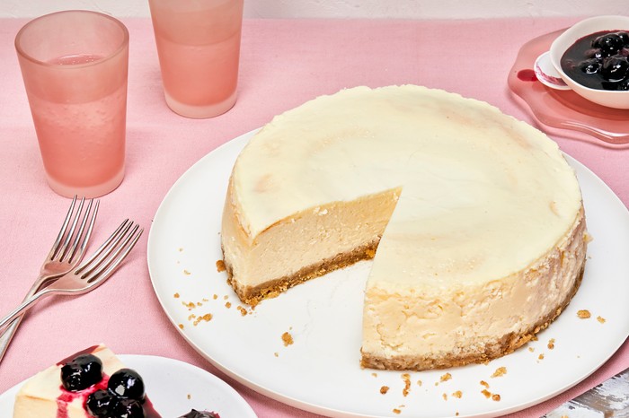 A white plate topped with a creamy cheesecake set against a pink background