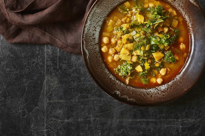 Two black bowls filled with green lentils and chickpeas in a broth