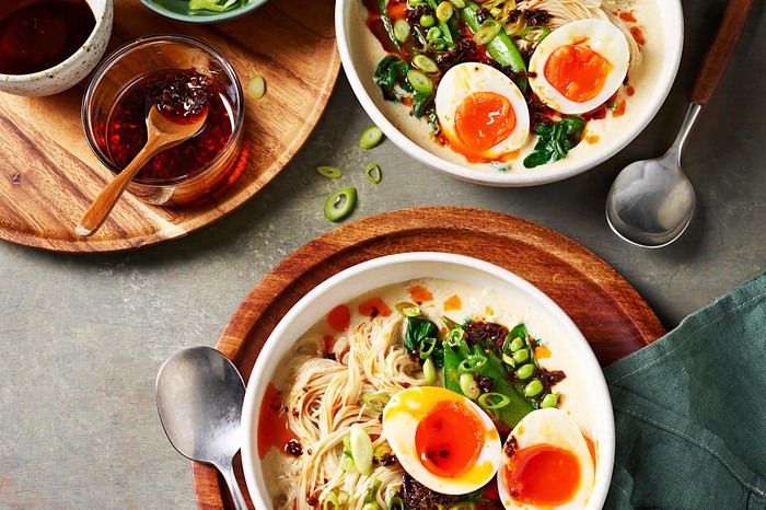 Two white bowls filled with noodles, green vegetable and eggs with a bright orange yolk