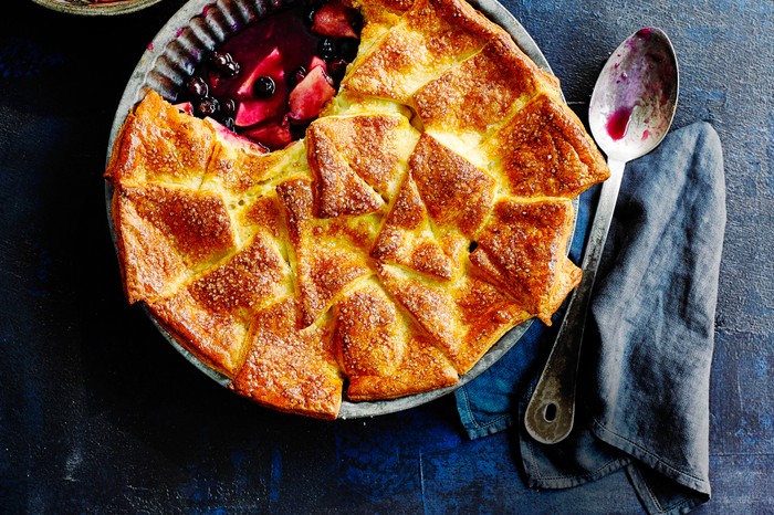 Apple and Blueberry Pie Recipe served in a metal pie dish and a large metal dessert spoon on a blue board