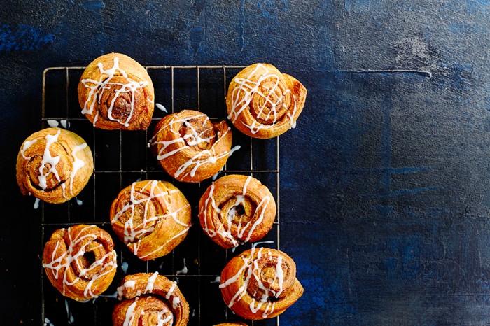 12 croissant cinnamon rolls served on a cooling rack on a dark blue board
