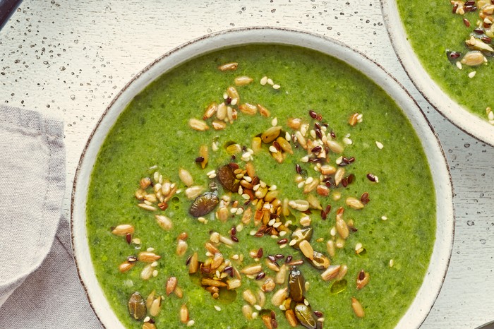 A bowl of leek, spinach and pea soup, topped with seeds