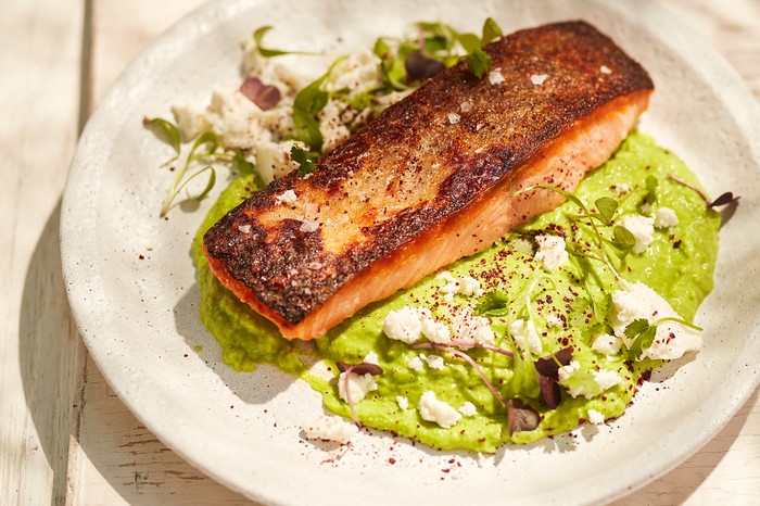 A fillet of salmon sat on a bed of green purée in the sun on cream plate