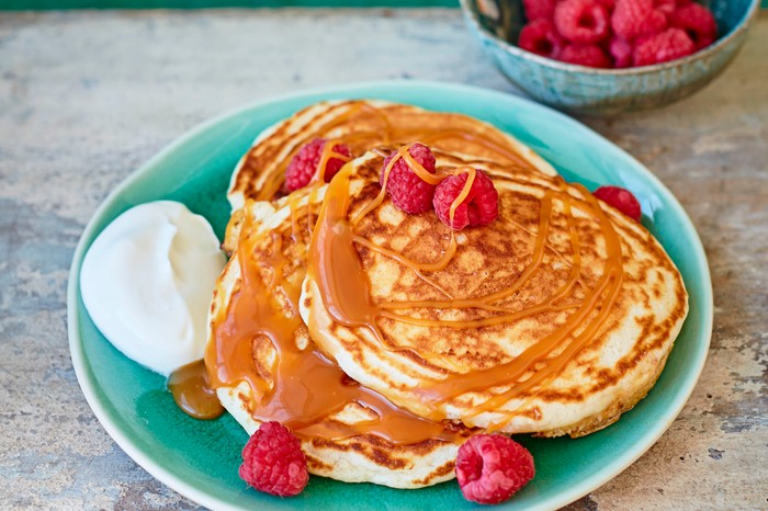 A pile of stuffed pancakes filled with salted caramel, served with raspberries