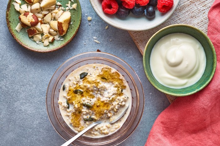 a bowl of oats next to plates of berries, yogurt and chopped nuts on a red napkin