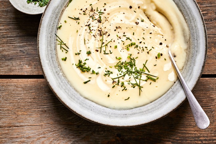 A grey bowl filled with creamy parsnip soup and topped with chopped chives