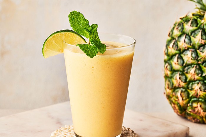 Glass of pineapple smoothie garnished with lime wedge and mint, next to a pineapple