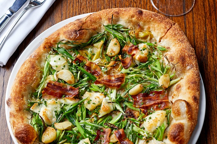 A puffy pizza base topped with greens, goat's cheese and crispy pancetta