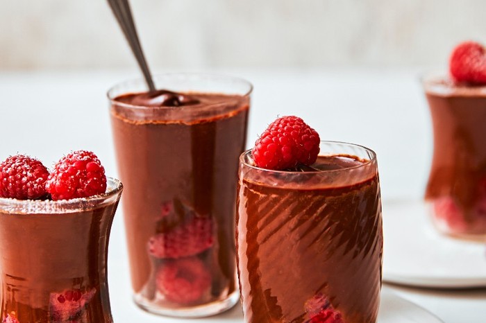Tall glasses filled with chocolate mousse and topped with raspberries on a grey background
