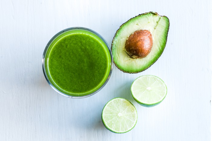 Avocado and limes alongside a glass of green smoothie