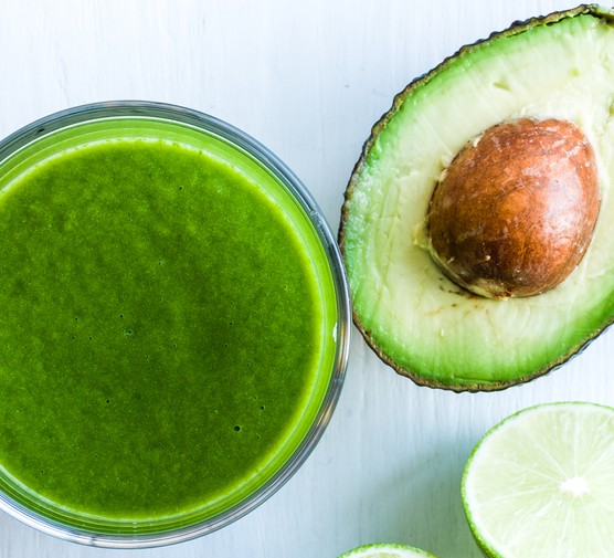 Avocado and limes alongside a glass of green smoothie