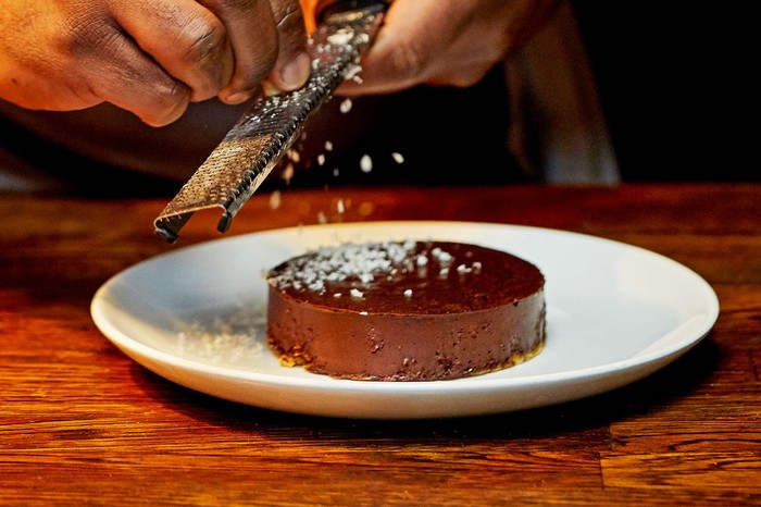 A man in an apron grating chocolate onto a chocolate torte