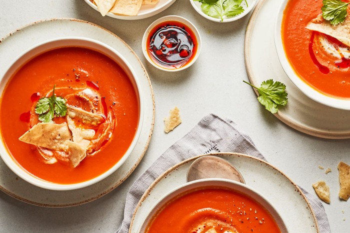Tomato soup in three bowls topped with coriander and tortilla chips