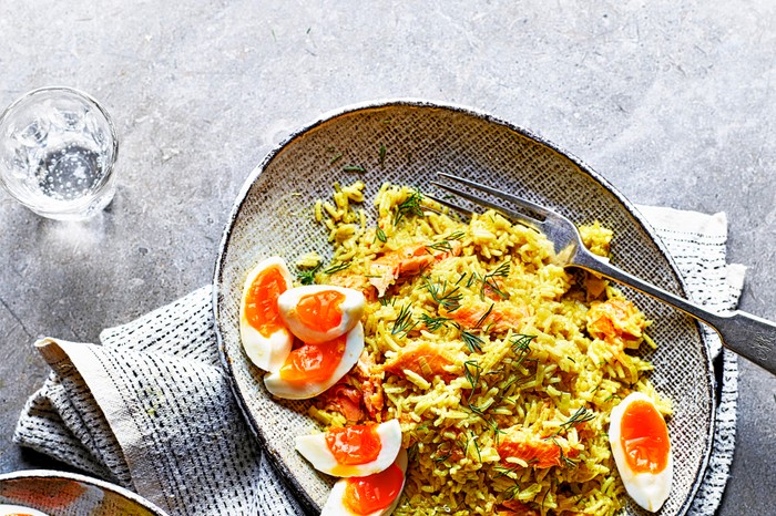 Smoked trout kedgeree with leeks on a grey oval plate served with boiled eggs sliced into quarters